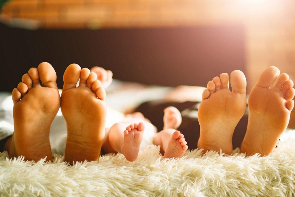 soles of two pairs of adult feet on either side of a pair of baby feet